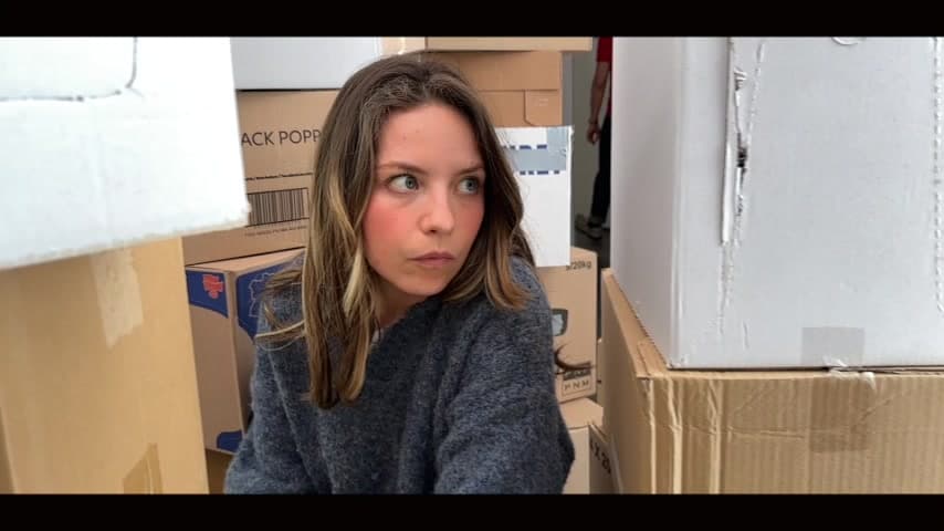 A woman sitting among cardboard boxes and looking to the right