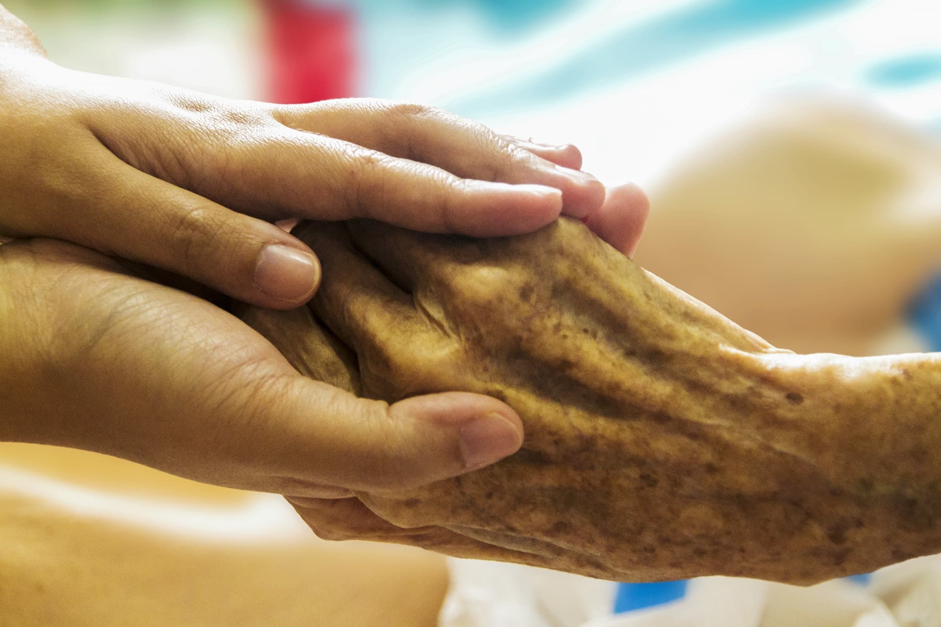Two pairs of hands holding each other. One pair is a younger person, the other pair is an older person.